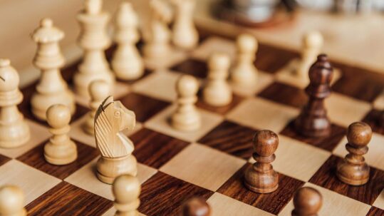 Holzschachfiguren auf einem Schachbrett als Symbol für Strategie und Taktik beim Bieterverfahren im Immobilienkauf | Bieterverfahren