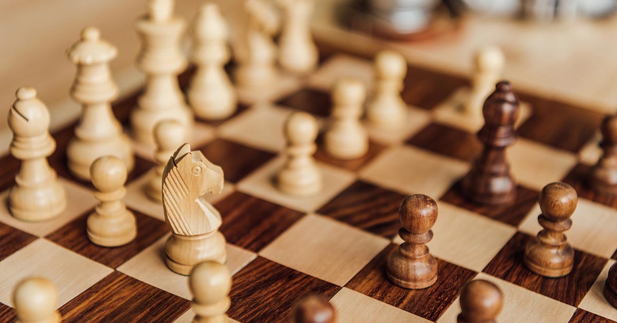 Holzschachfiguren auf einem Schachbrett als Symbol für Strategie und Taktik beim Bieterverfahren im Immobilienkauf | Bieterverfahren